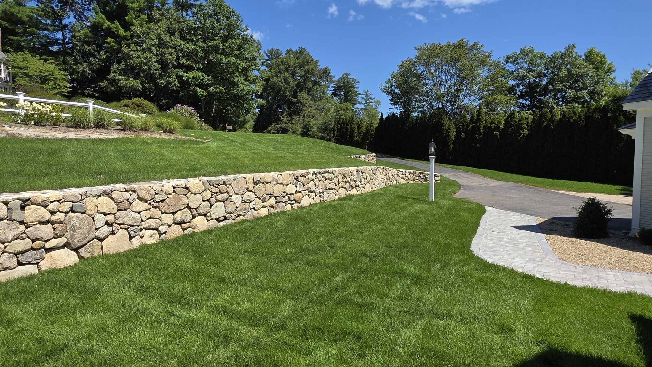 Long natural-stone wall built across a landscaped Norwell property