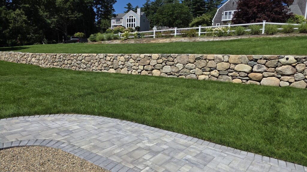 Natural-stone wall and curved walkway across a Norwell property