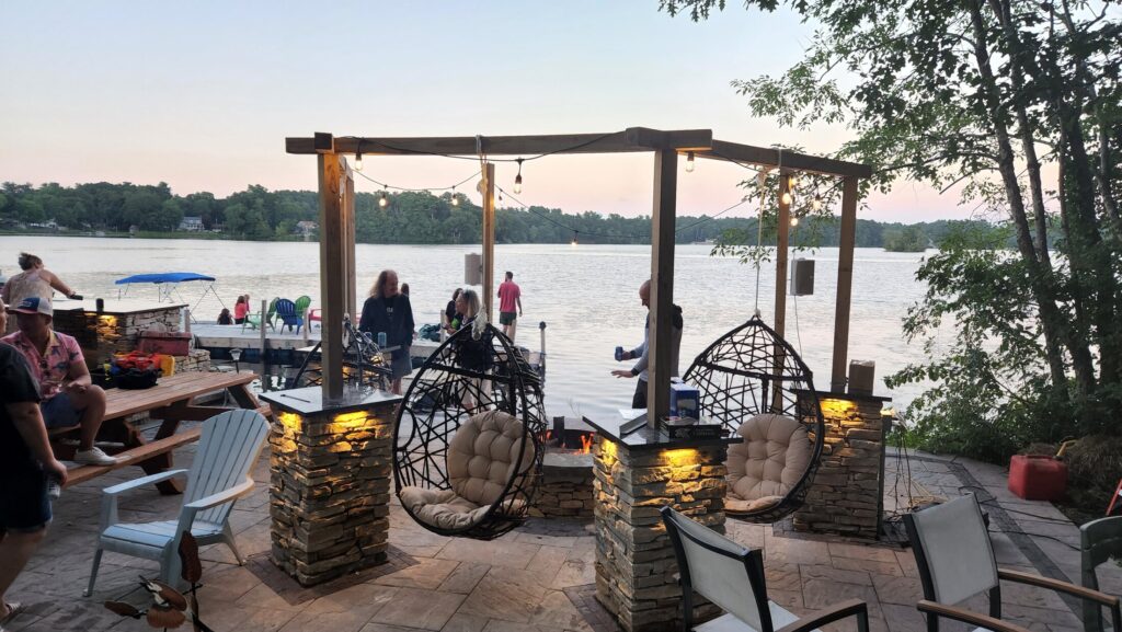Waterfront patio with illuminated stone pillars and suspended seating at sunset