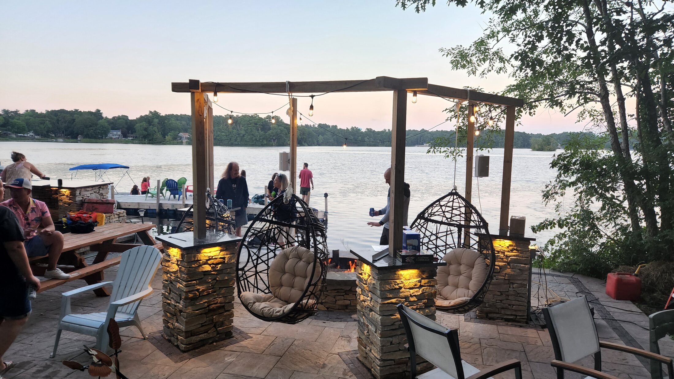 Waterfront patio with illuminated stone pillars and suspended seating at sunset